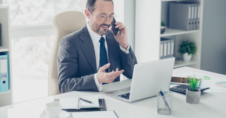 Professional man in suit and tie on phone and using laptop.